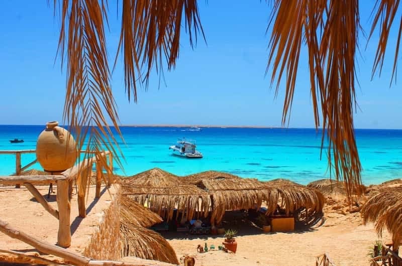 مظلات من القش ومقاعد خشبية تطل على البحر الفيروزي في جزيرة مقاويش