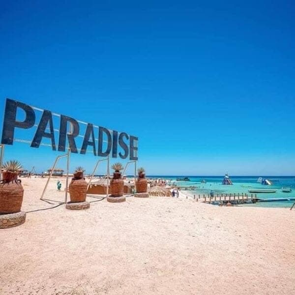 Large Paradise letters on the beach with parasols behind