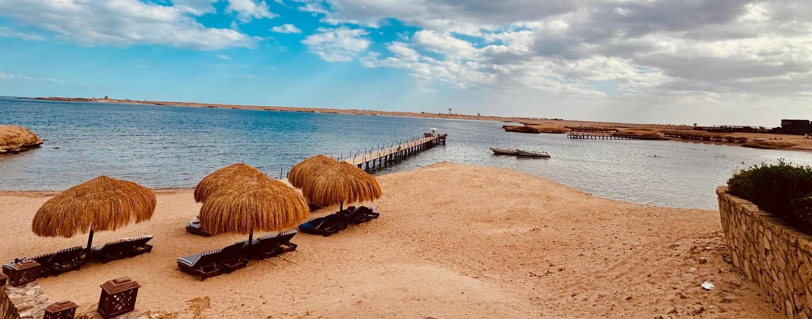 مظلات من القش على شاطئ شرم النقا والرصيف الخشبي ممتد في الخليج